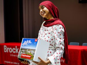 A Niagara Principal’s Scholarship recipient smiles while holding a Brock welcome box on stage.