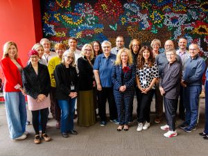 A large group of university staff pose together in front of a colourful floral mural during a Provost Summit gathering.