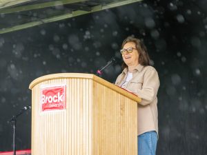 A speaker gives opening remarks from a Brock University podium on an outdoor stage as rain falls during the Rankin Cancer Run.