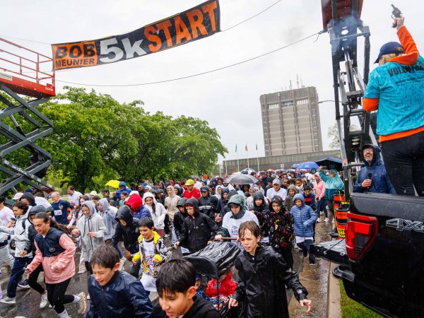 Crowd of children and adults run through heavy rain under the ‘Bob Meunier 5K Start’ banner as volunteers cheer them on from a pickup truck at the Rankin Run.