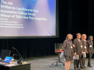 Students stand on a stage under theatre light.