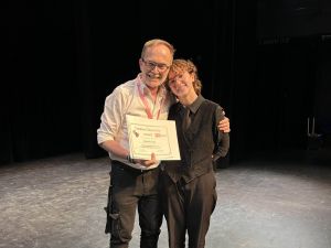Two people stand together smiling at the camera.
