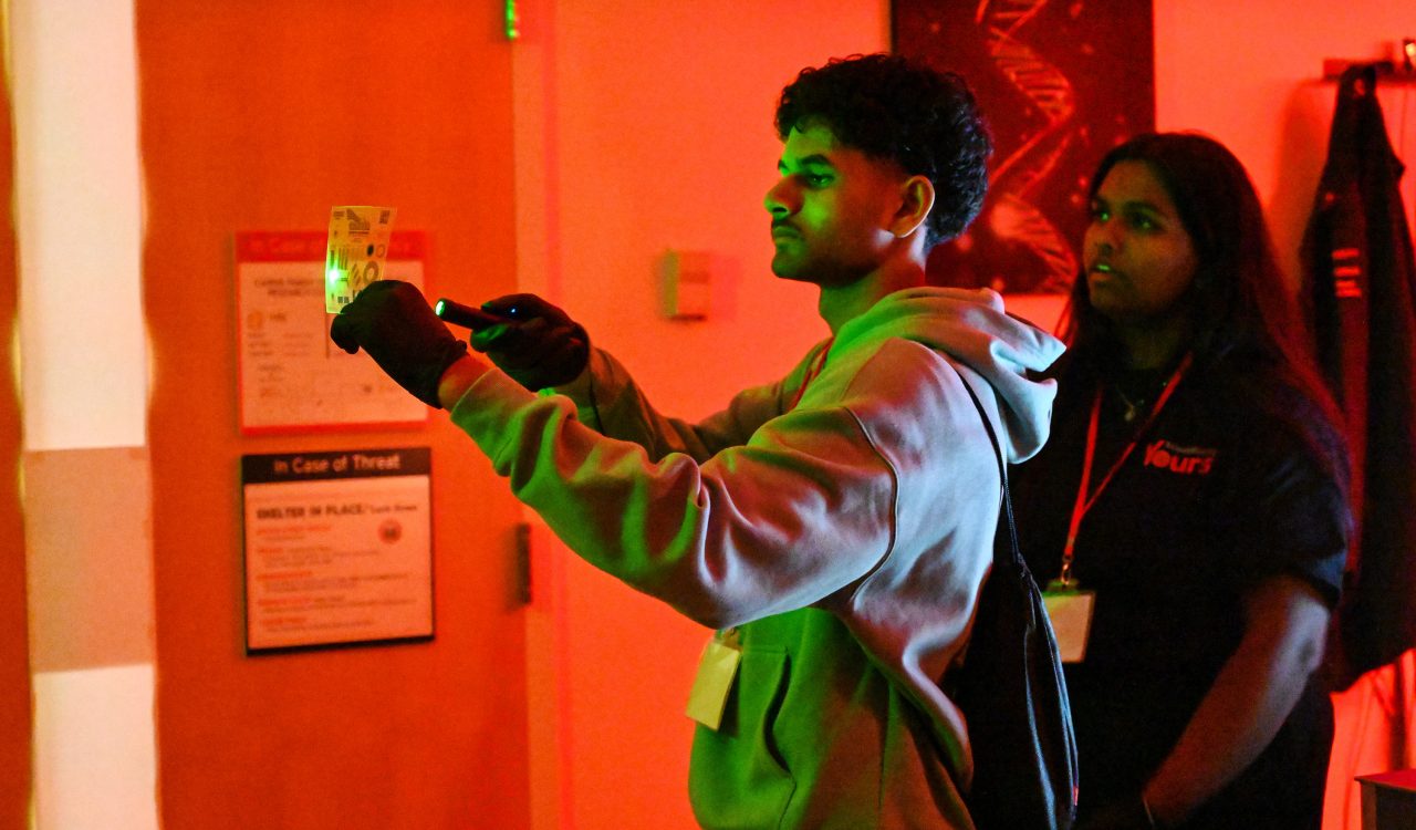 A high school student shines a flashlight on an object in a dark room.
