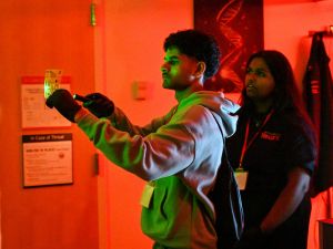 A high school student shines a flashlight on an object in a dark room.