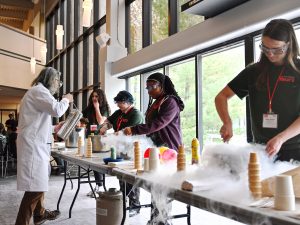 An instructor pours a liquid from a canister while students help to mix the ingredients in a bowl.