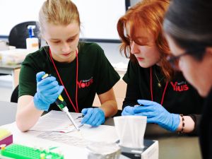 There is a high school student observing a chemical reaction with another observer close by.
