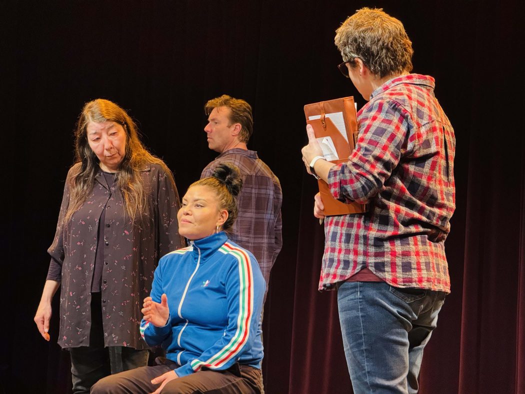 Four actors stand on stage together under stage lights.