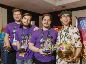 A group of four students hold video game controllers and a disco ball standing together at an event.