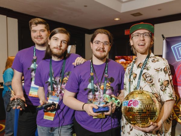 A group of four students hold video game controllers and a disco ball standing together at an event.