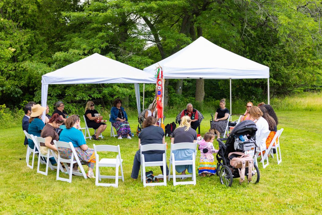 Invited guests seated in a circle of white chairs on the grassy knoll during the Naming Ceremony.