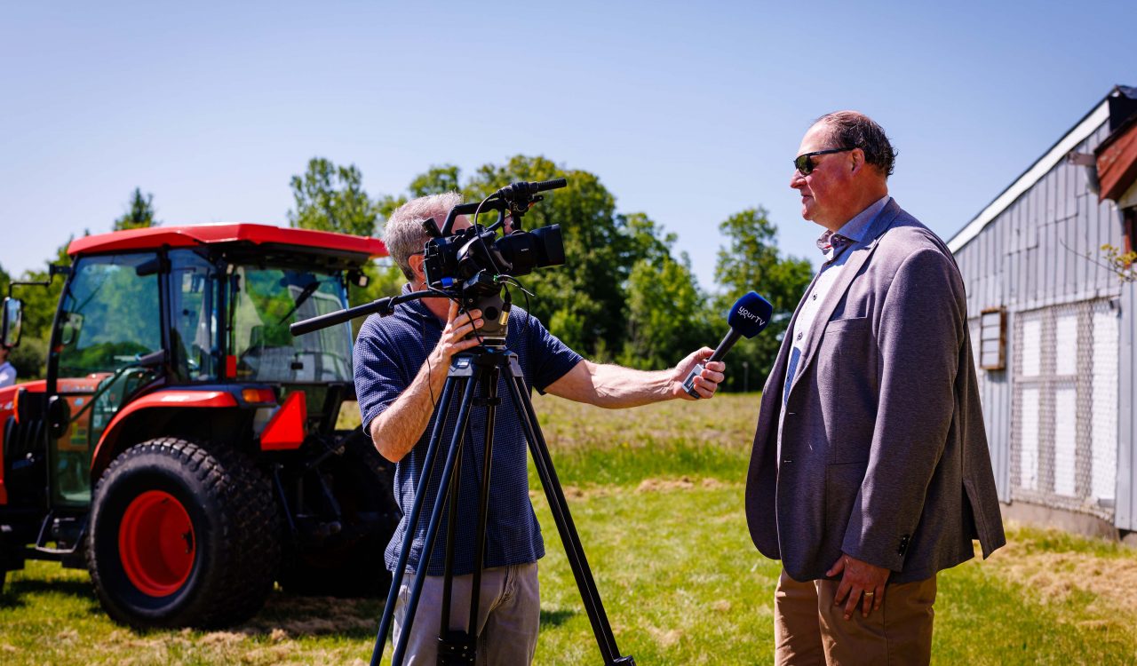 A man standing behind a camera interviews another man for a news story.