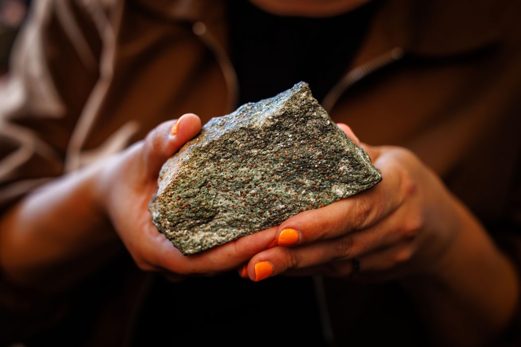 Close-up of Tanya Kizovski’s hand holding a grey rock with red dots sprinkled throughout the rock sample.