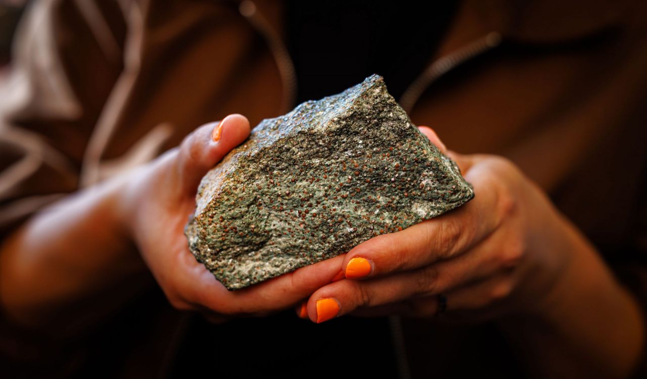 Close-up of Tanya Kizovski’s hand holding a grey rock with red dots sprinkled throughout the rock sample.