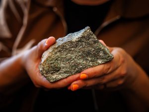 Close-up of Tanya Kizovski’s hand holding a grey rock with red dots sprinkled throughout the rock sample.
