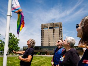 A group of people raise a pride flag outside a tall building.