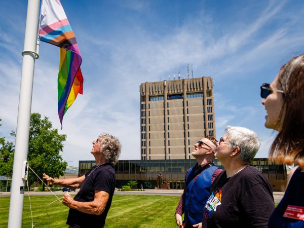 A group of people raise a pride flag outside a tall building.