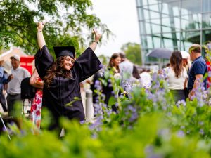 A smiling young woman in academic robes poses for a photo outside after a university graduation.