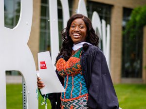 A smiling young woman holding a diploma poses for a photo at a university graduation.
