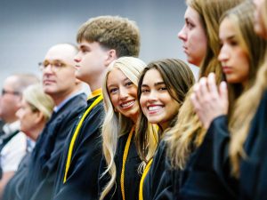 Young people in academic robes smile at a university graduation ceremony.