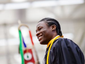 A young man in an academic gown smiles at a university graduation ceremony.
