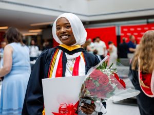A smiling young woman holding flowers poses for a photo at a university graduation.