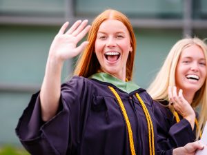 Two smiling young woman in academic robes outside a university graduation.