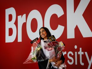 A smiling young woman holding flowers poses for a photo at a university graduation.