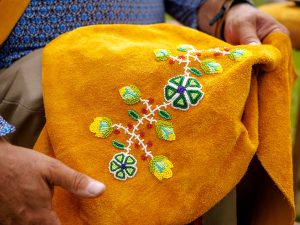 A person holds a piece of soft golden beige leather adorned with a floral pattern in greens, yellows, red and purple.