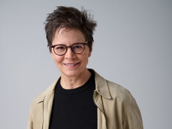 A woman stands smiling with her hands in her pockets.