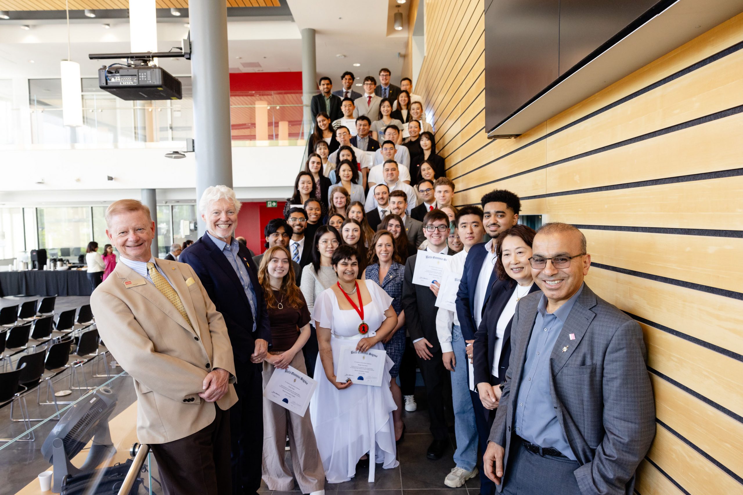A large group of smiling people stand on a staircase to take a group photo to mark a recognition.