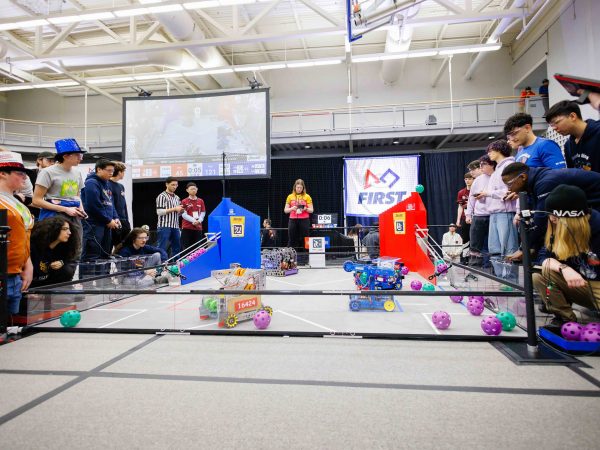 A group of people control robots that are seen moving around in a marked ring.