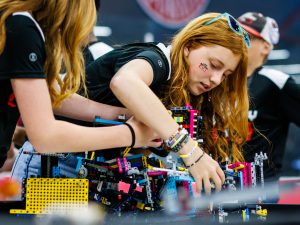 Two girls are repairing their student-built robot in between matches at a robotics competition.