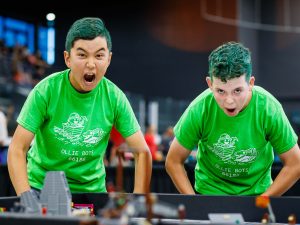 Two boys dressed in green team t-shirts with green hair pose with animated facial expressions