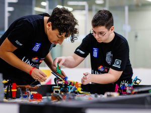 Two girls repair their student-built robot in between their matches at a robotics competition.