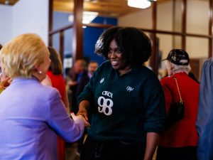 Two women shake hands while speaking to one another.