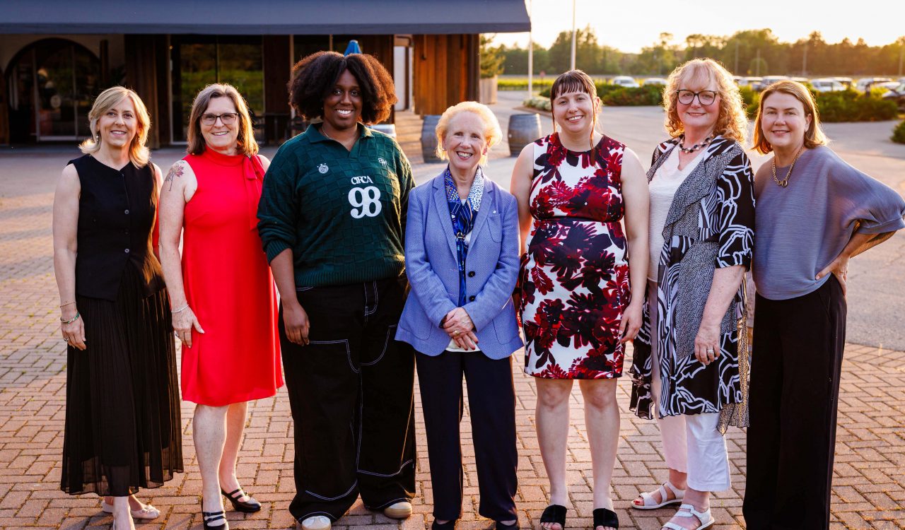 Seven women stand together outside.