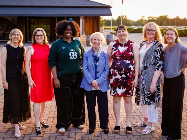 Seven women stand together outside.