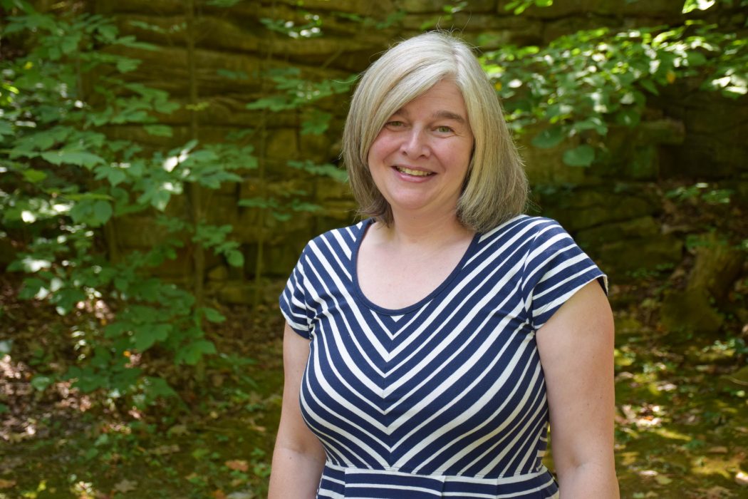 Karen Louise Smith in a striped dress near in front of a tree.