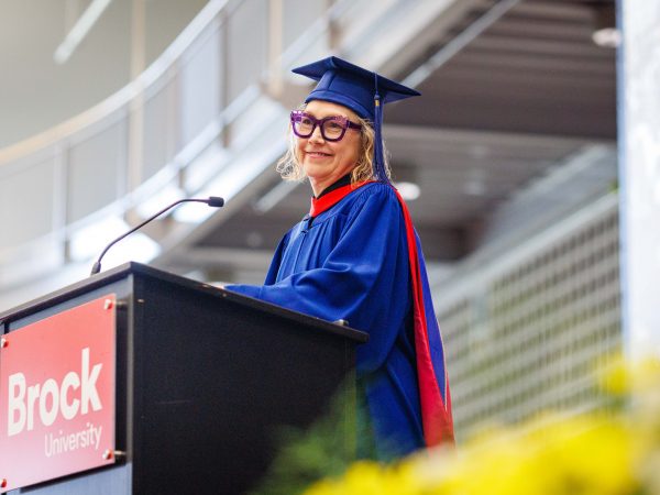 A woman in a Convocation gown stands at a podium smiling.