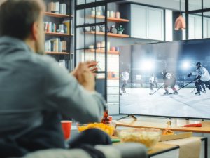 A man, seen from behind, watches ice hockey on a TV.