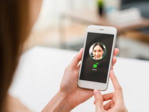 A woman holds a smartphone showing a photo of her face to unlock the device.