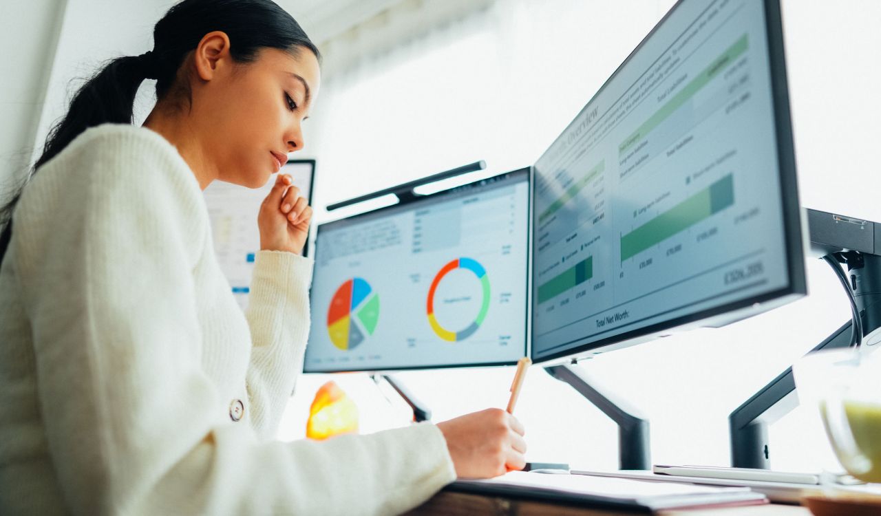 A woman works at a computer using two monitors showing various graphs.