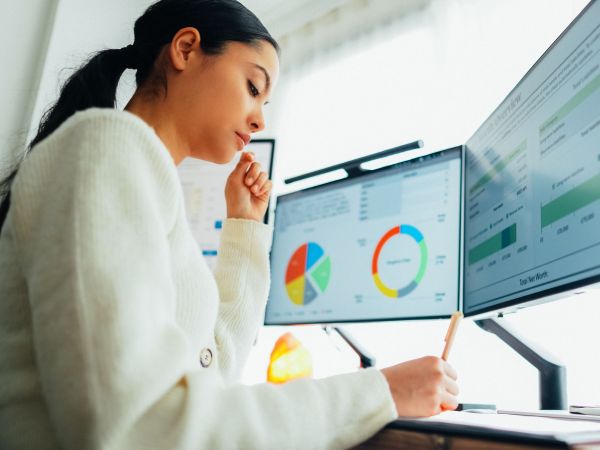 A woman works at a computer using two monitors showing various graphs.