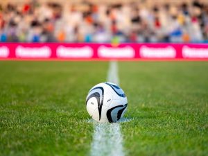 A soccer ball on the halfway line with a crowd in the background.