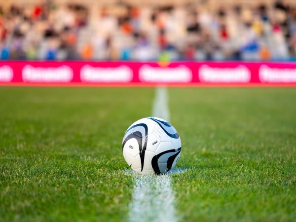 A soccer ball on the halfway line with a crowd in the background.