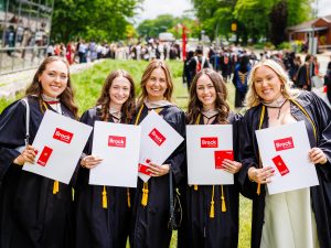 A group of new university graduates pose for a photo with their diplomas.
