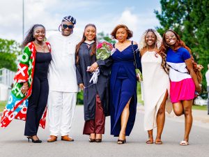 A woman in an academic robe poses with a group of loved one after a university graduation ceremony.