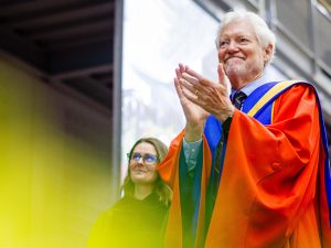 A man in academic regalia applauds during a university graduation ceremony.