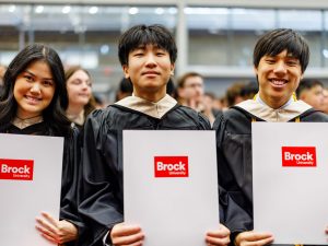 Three new university graduates pose for a photo with their diplomas.