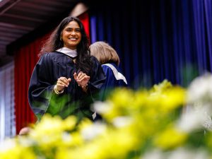 A young woman in an academic robe smiles while crossing the stage during a university graduation ceremony.